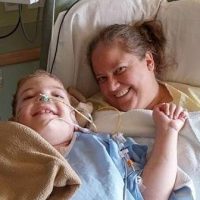 A smiling mother, Marie Jackson, lies in a hospital bed beside her young son, Maxx, who is also smiling while connected to a nasal cannula and medical tubing. Marie, a Montessori school teacher and devoted mother of three, faced the heartbreaking child loss of Maxx, who was born with significant medical challenges and passed away at age nine in 2016 from a brain hemorrhage. His organ donation saved three other lives, offering hope in grief. Marie lives in Janesville, Wisconsin, with her two daughters and their cat, and is an active member of a GPS Hope Share & Care group. GPS Hope - Grieving Parents Sharing HOPE.