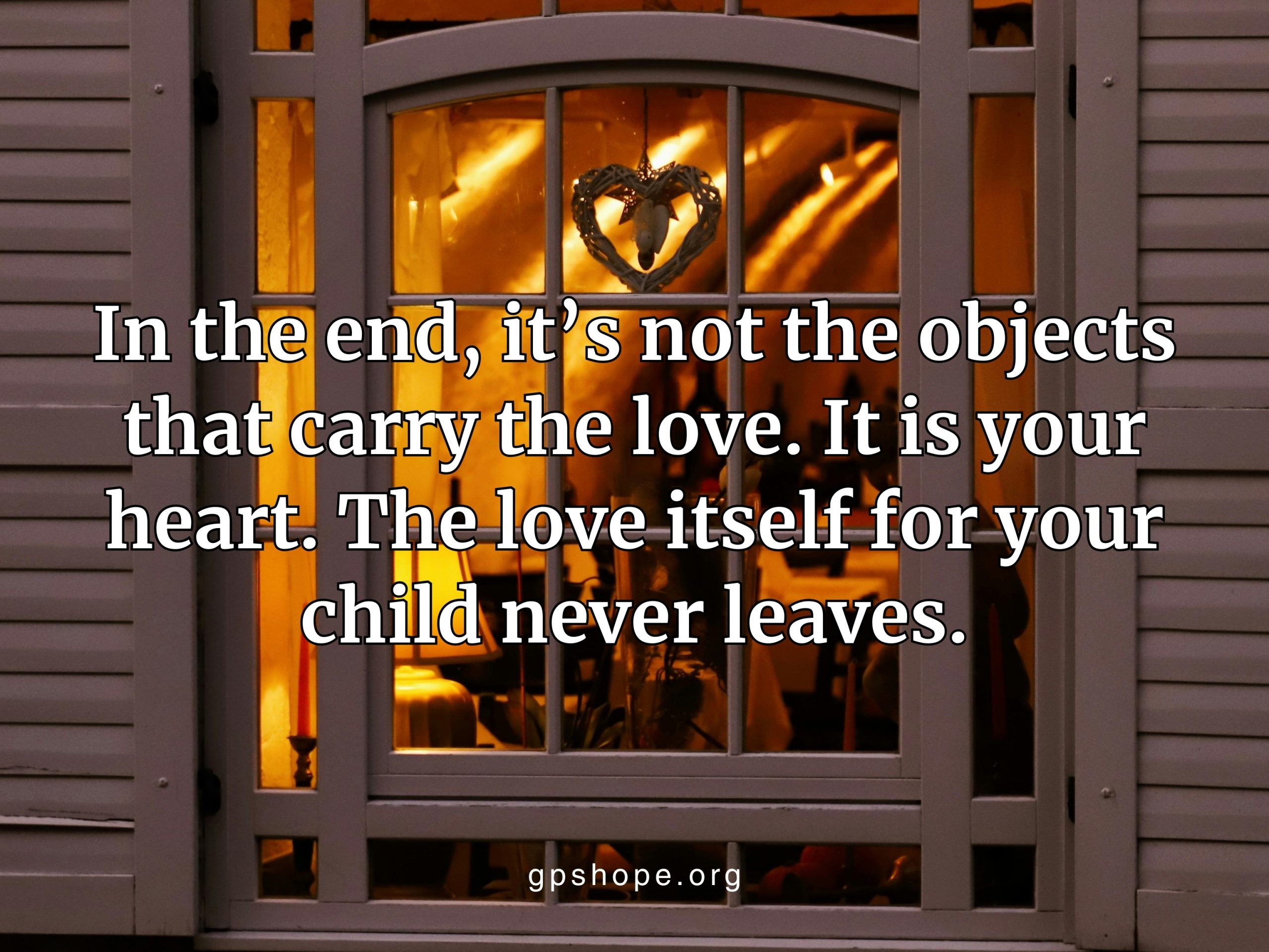 A dimly lit window with a heart-shaped wreath, reflecting Sacred Reminders that love for a child never leaves but lives on in the heart. GPS Hope – Grieving Parents Sharing HOPE.