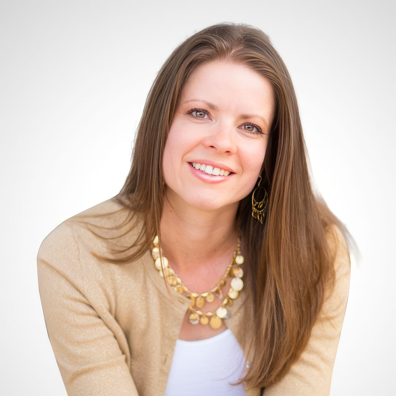 Portrait of a smiling woman with long brown hair wearing a gold cardigan and statement necklace, representing hope and strength in the journey of No Rainbow Baby after Pregnancy Loss. GPS Hope - Grieving Parents Sharing HOPE.